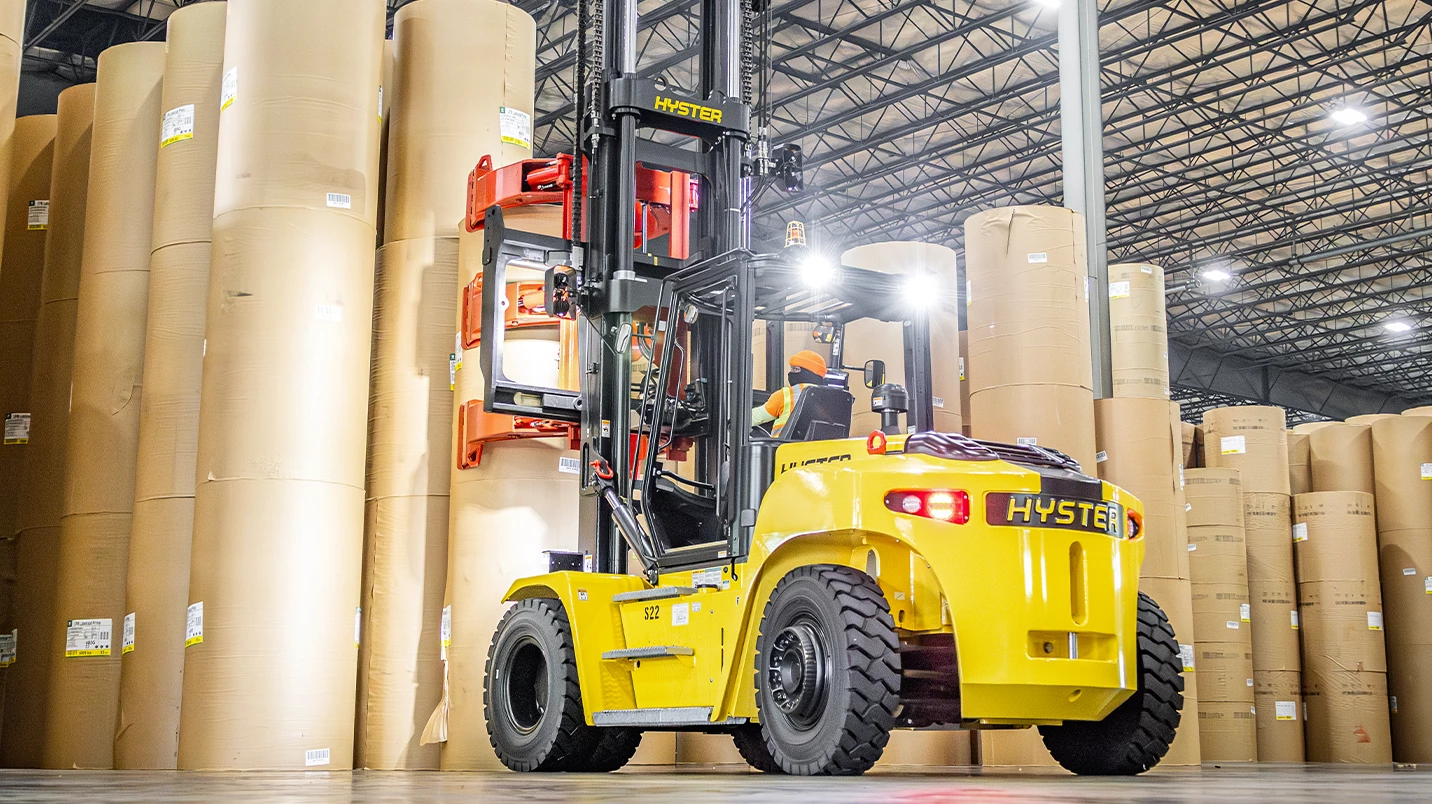 Lift truck driver operating a Hyster lift truck with a Bolzoni pallet attachment.