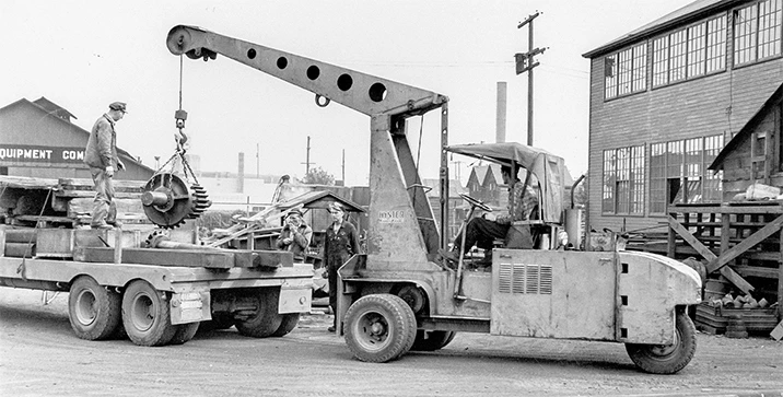 1940’s mobile crane unloading machine parts from truck.